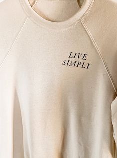 One of our favorite mantras, now available in our oh-so-cozy sweatshirts! The minimal design will pair effortlessly with just about any bottoms - leggings, denim, shorts - you name it! The neutral tone keeps things light + airy yet appropriate for every season. For chilly summer evenings and warm winter layers, sweatshirts are a staple item all year round. The NuBlend® fleece is pre-shrunk, pull-resistant, and quarter-turned so it won't crease in the middle. Made from 50% polyester and 50% susta Relaxed Fit Basic Sweatshirt With Text Print, Relaxed Fit Crew Neck Hoodie With Screen Print, Relaxed Crew Neck T-shirt With Screen Print, Luxury Men's Outdoor Sweatshirt, Cotton Sweatshirt With Embroidered Text, Relaxed Fit, Winter Layering, Live Simply, Summer Evening, Cozy Sweatshirts