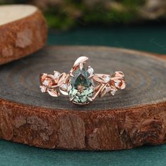 an engagement ring with a green stone surrounded by white diamonds on top of a tree stump