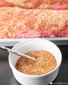 a white bowl filled with spices next to a meat roasting pan on a table