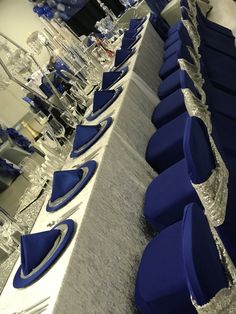 rows of blue chairs lined up along a long table with silver sequins on it