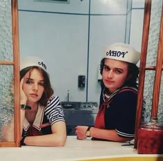 two young people sitting at a counter in front of a window wearing sailor's hats