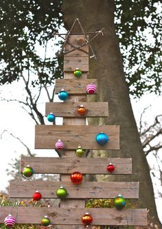 a wooden christmas tree with ornaments hanging from it's sides in front of a tree