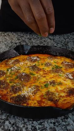 a person reaching for a piece of food in a skillet on a granite counter top