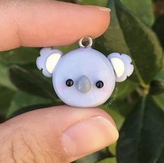 a person holding a tiny white bear with black eyes on it's face in front of some green leaves