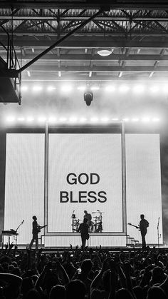 black and white photograph of band performing on stage with god bless sign in the background