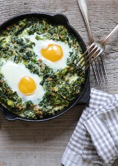 two fried eggs on top of spinach in a skillet with silverware next to it