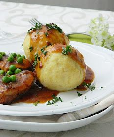 a white plate topped with meat covered in gravy and green peas next to a fork