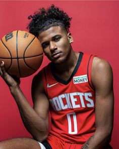 a man holding a basketball in his right hand and sitting on the floor next to a red wall