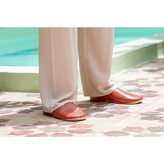 a person in white pants and red shoes standing on a tiled floor next to a pool