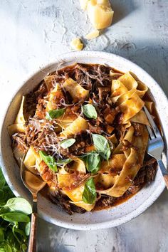 a white bowl filled with pasta and meat on top of a table next to some parmesan cheese