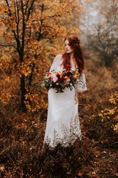 a woman in a white dress is walking through the woods with flowers on her wedding day