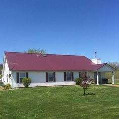 a white house with a red roof in the middle of a green yard and trees