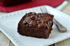 a piece of chocolate cake on a white plate with a fork and red napkin in the background