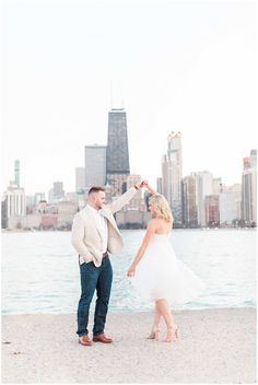 a man and woman standing next to each other near the water in front of tall buildings