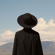 a person with a black hat standing in front of mountains