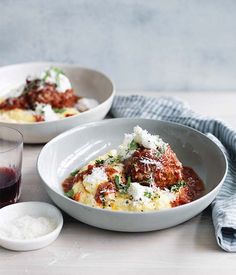 two white bowls filled with food on top of a table next to glasses and spoons