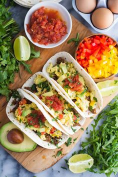 three breakfast tacos on a cutting board with avocado, salsa and eggs