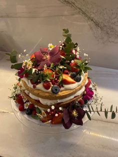 a three layer cake with berries, flowers and leaves on the top is ready to be served