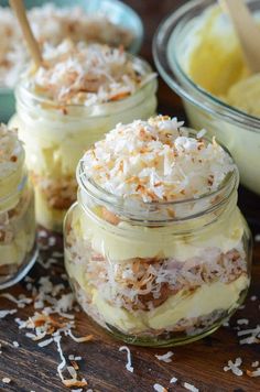 four jars filled with desserts sitting on top of a wooden table covered in coconut flakes