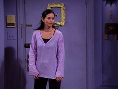 a woman standing in front of a door wearing a purple sweater and black pants with her hands on her hips