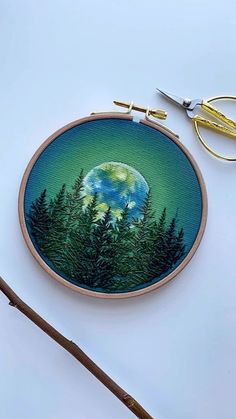 an embroidery project with some scissors and thread on the table next to it is a picture of trees