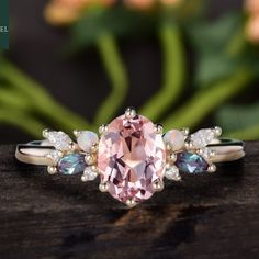 a ring with an oval shaped pink stone surrounded by smaller stones