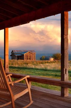 a wooden rocking chair sitting on top of a wooden deck next to a building with a barn in the background