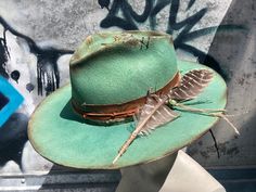 LADY JANE is a transformed Olive & Pique Kaia hat. It's structured, with a flat brim, and a 4.25" crown rise. The brim is 3 1/4 and the head size is adjustable up to 23" It's been reshaped, dyed, burned, stitched and etched with a paisley & floral design.  The band is etched deer leather, overlaid with silk, bandana, leather cord, and twine.  It's tied off with a large turkey feather and an African free trade bead. Please feel free to ask questions. Country Style Fedora For Kentucky Derby With Flat Crown, Flat Crown Hats For Kentucky Derby And Rodeo, Kentucky Derby Hats With Flat Crown For Country Events, Country Style Flat Crown Hat For Kentucky Derby, Rustic Curved Brim Hat For Kentucky Derby, Rustic Top Hat With Adjustable Flat Brim, Rustic Kentucky Derby Hat With Curved Brim, Fitted Wide Brim Rustic Hat, Fitted Country Hat With Flat Crown