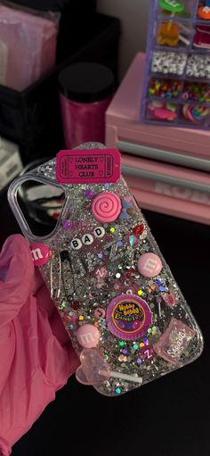 someone is holding up a phone case with glitter and buttons on the back, in front of some other items