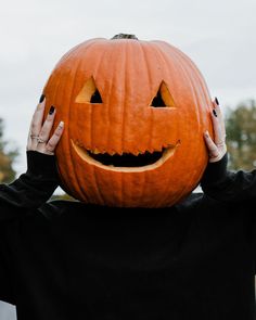 a person holding up a pumpkin to their face with both hands on top of it