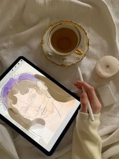 a person drawing on an ipad next to a cup of tea