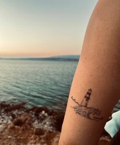 a person's arm with a lighthouse tattoo on it and the ocean in the background