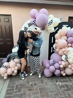 two people standing next to each other in front of a balloon arch with checkered balloons