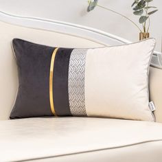 a white couch with a black and gold pillow on it next to a potted plant