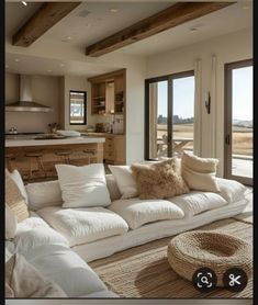 a living room filled with white furniture and lots of windows next to an open kitchen