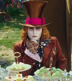 the mad hatter is sitting at a table with cupcakes