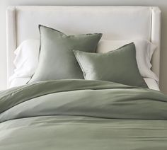 a bed with green sheets and pillows on it