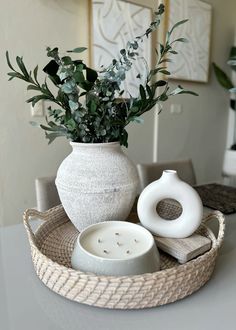 a white vase sitting on top of a table next to a bowl filled with flowers