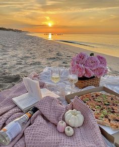 two pizzas and wine are on the beach with pink flowers in front of them