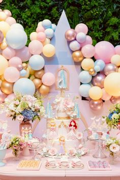 a table topped with lots of balloons and cake next to a castle covered in flowers