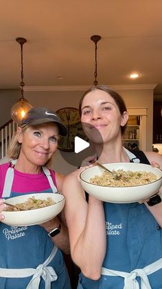 two women in blue aprons holding plates of food