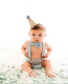 a baby wearing a blue bow tie and a party hat sitting on a white rug