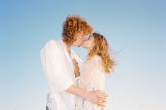 a man and woman standing next to each other in front of the ocean on a sunny day