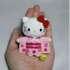 a hand holding a hello kitty doll in pink and white crocheted clothes with a red bow