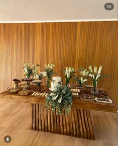 a table topped with lots of cakes and desserts next to a wall covered in wood paneling