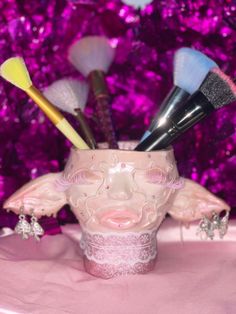 a pink vase filled with makeup brushes on top of a table