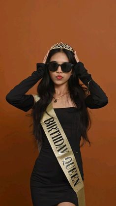 a woman in a black dress and gold sash with sunglasses on her head is posing for the camera