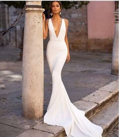 a woman in a white dress leaning against a pillar with her hands on her hips