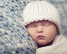 a newborn baby wearing a white knitted hat sleeping on a blue and white blanket