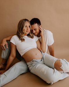 a pregnant couple sitting on the floor with their arms around each other and looking at the camera